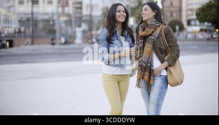 Two stylish smiling young women standing facing each other chatting outdoors in a town square head and shoulders in winter fashion Stock Photo