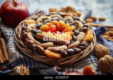 Composition of dried fruits and nuts in small wicker bowl placed on a stone table. Assortment contais almonds, walnuts, apricots, plums, figs, dates, Stock Photo