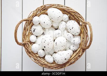 Basket of chicken and quail white dotted Easter eggs in brown wicker basket. Placed on white wooden table Stock Photo