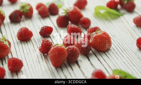 Bunch of fresh strawberries and ripe raspberries lying on surface of white timber tabletop near green leaves Stock Photo