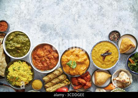 Composition of Indian cuisine in ceramic bowls on stone table. Tikka masala, butter chicken, Nilgiri, seekh kebab, rice, Onion Bhajia, paneer, samosa Stock Photo