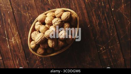 From above shot of bowl with whole fresh walnuts standing on scratched surface of wooden tabletop Stock Photo