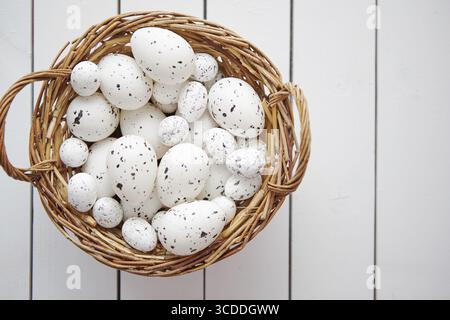 Basket of chicken and quail white dotted Easter eggs in brown wicker basket. Placed on white wooden table Stock Photo