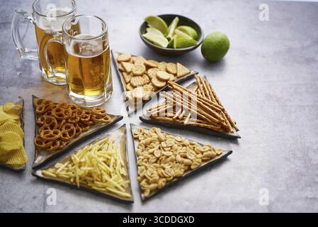 High angle of delicious various snacks fried potato chips, sticks, peanuts on table with glass of beer Stock Photo