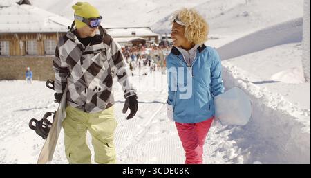 Young couple walking in heavy winter snow in a mountain ski resort carrying their snowboards Stock Photo