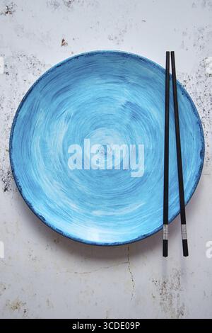Turquoise hand painted ceramic serving plate with wooden chopsticks on side. Flat lay, top view Stock Photo