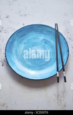 Turquoise hand painted ceramic serving plate with wooden chopsticks on side. Flat lay, top view Stock Photo