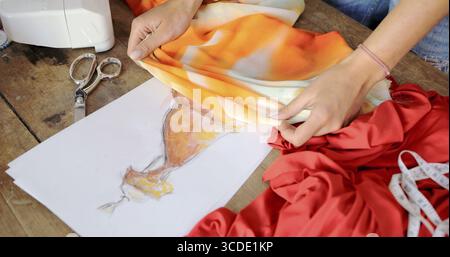 Crop female using sketch with drawn dress and choosing vibrant fabric in atelier Stock Photo