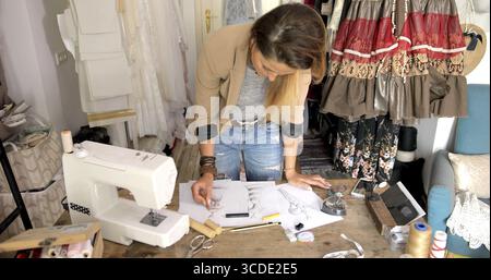 Female tailor standing near table in parlour and drawing sketch of dress Stock Photo
