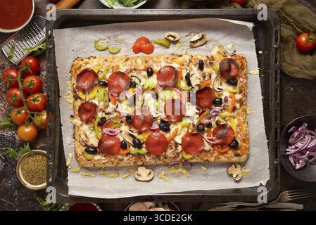 Delicious Homemade rectangular pepperoni pizza on a rustic table with ingredients. Top view, flat lay Stock Photo