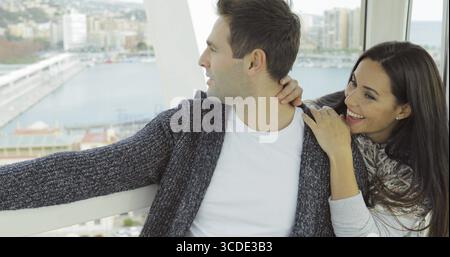 Young couple sitting arm in arm smiling as they go sightseeing on a cable car or ferris wheel getting an aerial view of the city and waterfront Stock Photo