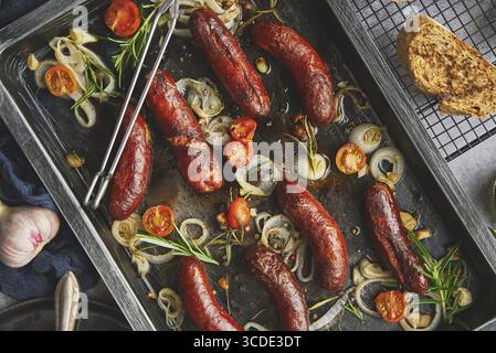 Delicious grilled sausages served on metal rusty tray. With barbecued vegetables, bread and mustard. Top view, flat lay Stock Photo