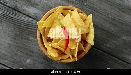 From above shot of bowl with crispy golden nacho chips with single red chili pepper on top served on wooden table Stock Photo