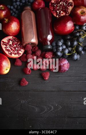Various fresh red, purple black fruits. Mix of fruits and bottled juices on black background. Selection of healthy vegetarian food, detox or diet conc Stock Photo