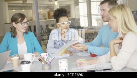 Casual man sitting with female coworkers at table and showing them folder with documents while discussing important issue Stock Photo