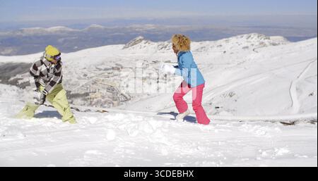 Young couple having fun playing in the winter snow on a mountain summit running and laughing Stock Photo