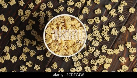 From above shot of bowl on wooden table filled with creative ornamental macaroni in mess around Stock Photo