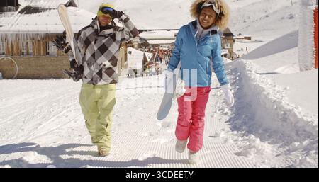 Young couple walking in heavy winter snow in a mountain ski resort carrying their snowboards Stock Photo