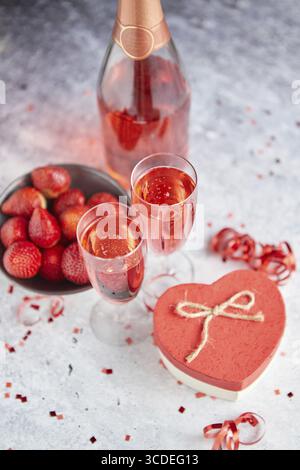 Bottle of rose champagne, two glasses with fresh ripe strawberries and heart shaped boxed gift, placed on stone table for a special romantic occasion Stock Photo