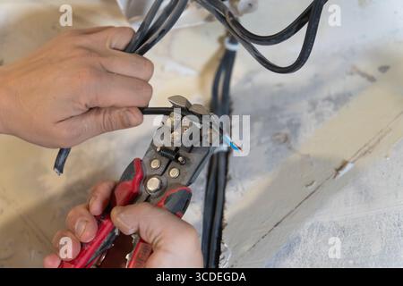 Close-up of electrician's hands using wire strippers to carefully remove insulation from electrical wires, preparing them for connection in electrical Stock Photo