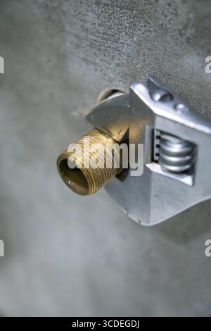 Close-up of plumber tightening brass pipe fitting using adjustable wrench, demonstrating precision and expertise in plumbing maintenance and repair. V Stock Photo
