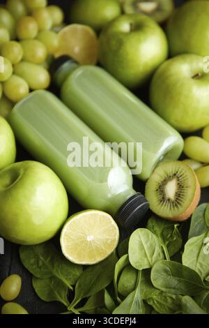 Fresh fruits and vegetables in green color concept. Placed with bottles of smoothie or juice on black wooden table Stock Photo