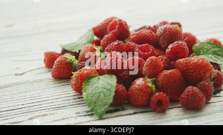 Small green leaves decorating pile of yummy ripe strawberries and raspberries lying on white lumber table Stock Photo