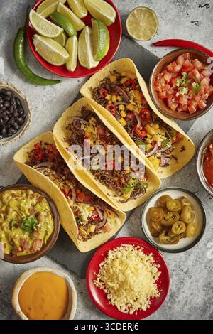 Tasty Mexican meat tacos served with various vegetables and salsa. With sides in ceramic bowls around. Top view composition Stock Photo