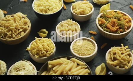 From above view of uncooked macaroni of different shape placed in white bowls on gray background Stock Photo