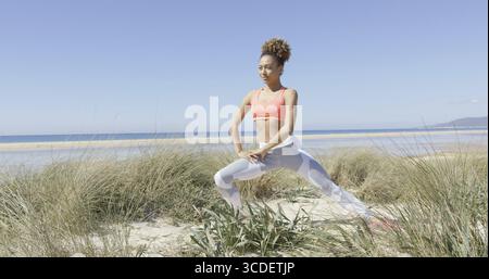 Young sporty woman stretching on a beach of Tarifa in Cadiz, Spain. Horizontal outdoors shot Stock Photo