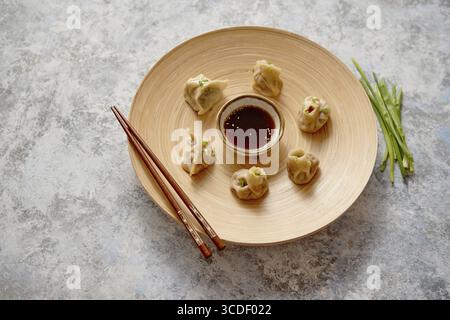 Delicious chinese dumplings served on wooden plate with chopstick and soy sauce in the middle. Placed on stone background with copy space. Chive od si Stock Photo