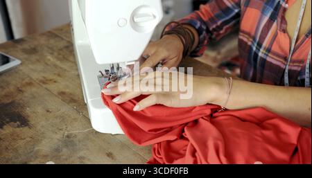 Crop faceless shot of female tailor using sewing machine and making dress with vibrant fabric Stock Photo
