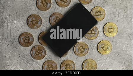 Top view of golden bitcoins composed on gray surface with modern smartphone on top Stock Photo