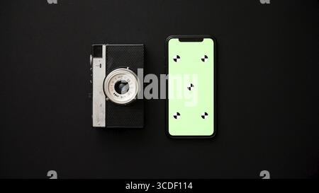 Old retro film camera and modern smartphone next to each other lying on black background. Top view Stock Photo