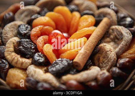 Close up of mix of dried fruits in a small wicker basket on wooden table. Assortment contais apricots, plums, figs, dates, cherries, peaches. Above vi Stock Photo