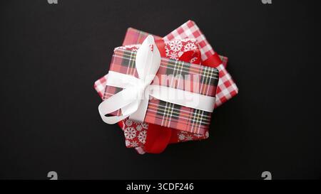 Stack of gifts boxes wrapped with red checkered pattern christmas paper with white bow on black table, top view Stock Photo