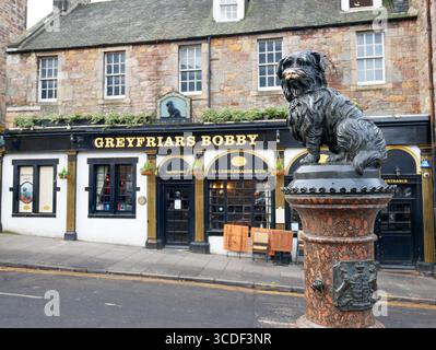 Bronze statue of Greyfriars Bobby with Greyfriars Bobby bar behind on Candlemaker Row behind Greyfriars Kirkyard in Edinburgh, Scotland. Stock Photo
