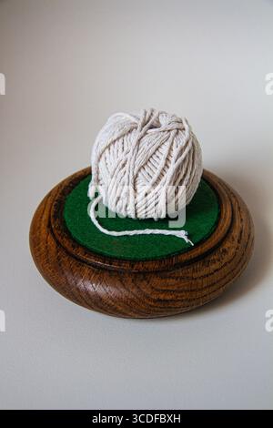 Minimalist still life of a ball of white string placed on a circular wooden drink mat on a plain background with shadow Stock Photo
