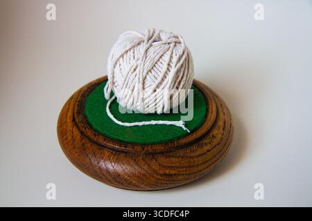 Minimalist still life of a ball of white string placed on a circular wooden drink mat on a plain background with shadow Stock Photo