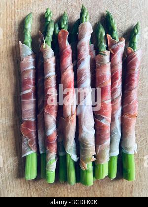 Fresh young asparagus wrapped in prosciutto meat on a wooden background. Directly above. Stock Photo