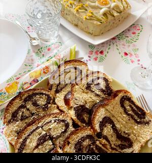 Cozonac, Romanian traditional Easter or Christmas sweet bread dessert. Cutting sweet bread on a plate and Russian salad on background. Directly above. Stock Photo