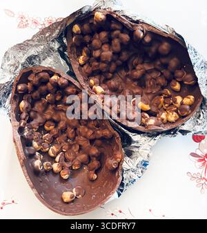 Chocolate Easter egg. Two halves of a chocolate Easter egg filled with hazelnuts on aluminum foil silver background. Easter and holidays. Close-up. Stock Photo