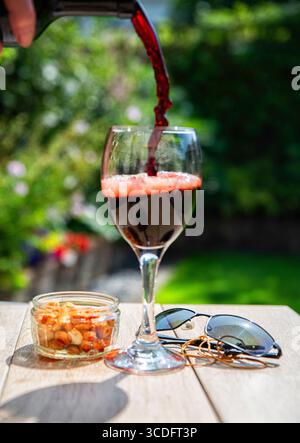 A glass of red wine being poured against a sunny garden setting Stock Photo