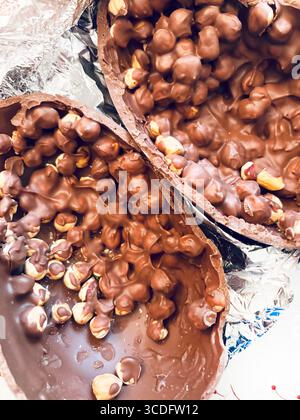 Chocolate Easter egg. Two halves of a chocolate Easter egg filled with hazelnuts on aluminum foil silver background. Easter and holidays. Close-up. Stock Photo