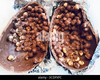 Chocolate Easter egg. Two halves of a chocolate Easter egg filled with hazelnuts on aluminum foil silver background. Easter and holidays. Close-up. Stock Photo
