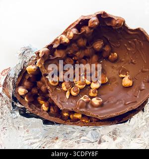 Chocolate Easter egg. Two halves of a chocolate Easter egg filled with hazelnuts cracked in pieces on aluminum foil background. Easter and holidays. Stock Photo
