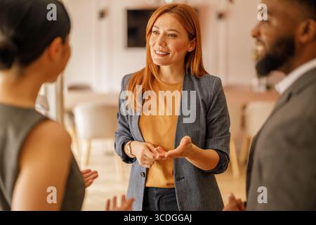 Smiling female manager discussing and explaining project strategies with business colleagues in office Stock Photo