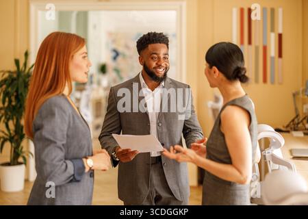Smiling male entrepreneur explaining business plan to female colleagues in collaborative office meeting Stock Photo