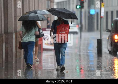 People make their way through the rain in Aldgate, London. Weather warnings have been issued as the fourth heatwave of the summer brings thunderstorms and showers. Picture date: Wednesday August 13, 2025. Stock Photo
