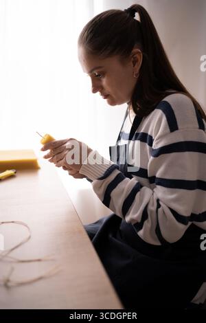 Hispanic woman in apron making beeswax candles using natural wax sheet. Side view. Close-up Stock Photo